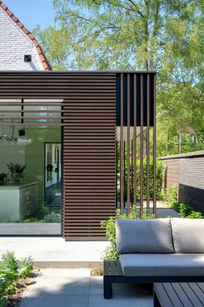 Een foto van een moderne uitbouw aan een jaren 30 woning. De gevel is bekleed met houten lamellen en grote glazen puien.