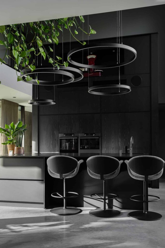 Villa woning in Bemmel met een gevlinderde betonvloer van Willem Designvloeren gecombineerd met een zwarte keuken en een zwart kookeiland met hieraan 3 barkrukken.