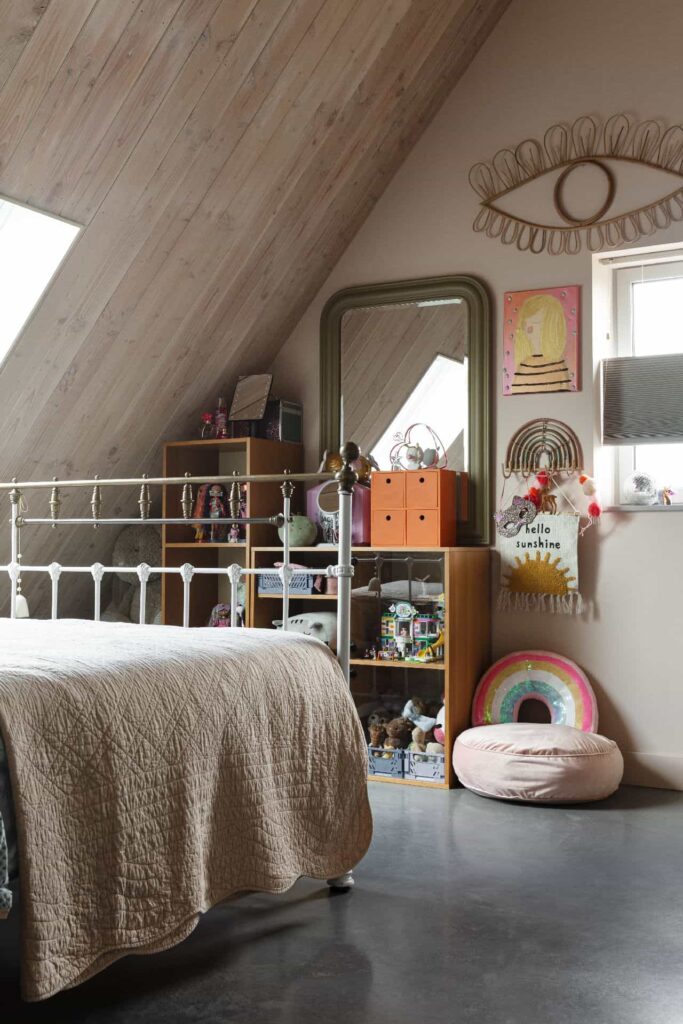 Slaapkamer in Brandwijk met daarin een gevlinderde betonvloer. In de kamer staan en hangen verschillende kleurrijke accessoires.