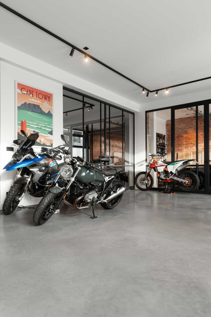 Woning in Den Haag met een gevlinderde betonvloer. Op de betonvloer staan 3 motors. Achter de stalen deur staat een Porsche.