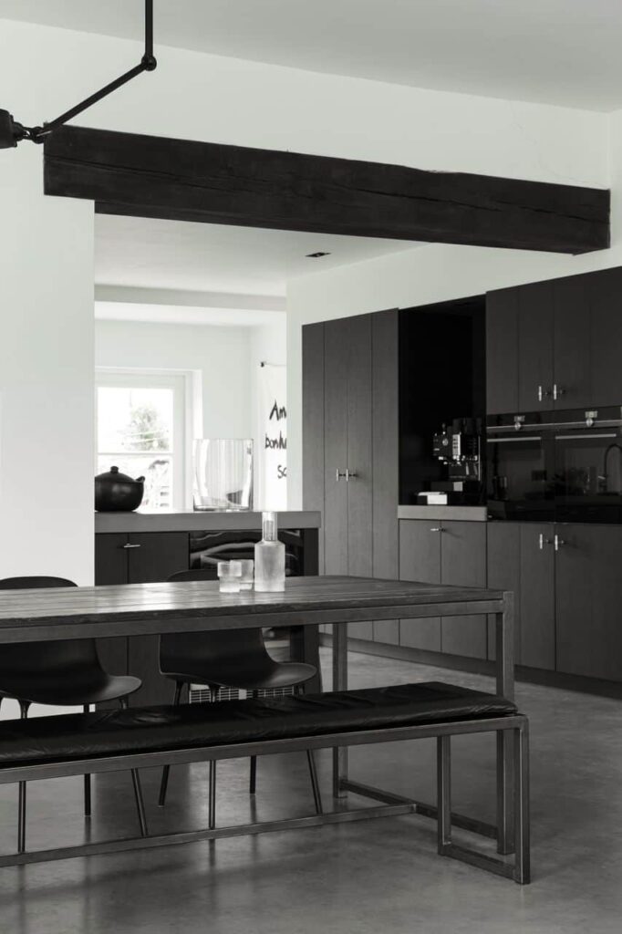 Zwarte houten keuken in Gieterveen met een houten tafel en hieraan zwarte stoelen. Gecombineerd met een gevlinderde betonvloer.