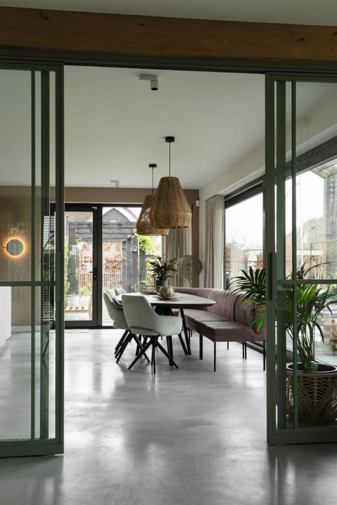 Eetkamer in Veenendaal met een zwarte tafel en daaraan grijze stoelen en een roze bankje. Dit staat op een gevlinderde betonvloer.