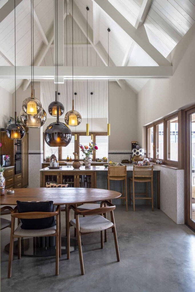 Keuken in Ulvenhout waarbij er veel gebruik gemaakt is van houten elementen. Zo is de keuken van hout, de ronde eettafel van hout en de stoelen en de barkrukken zijn ook van hout. Dit is gecombineerd met een gevlinderde betonvloer. De keuken heeft een hoog wit plafon wat in een punt loopt, hieraan hangen lange, ronde lampen. Beton laten storten kosten