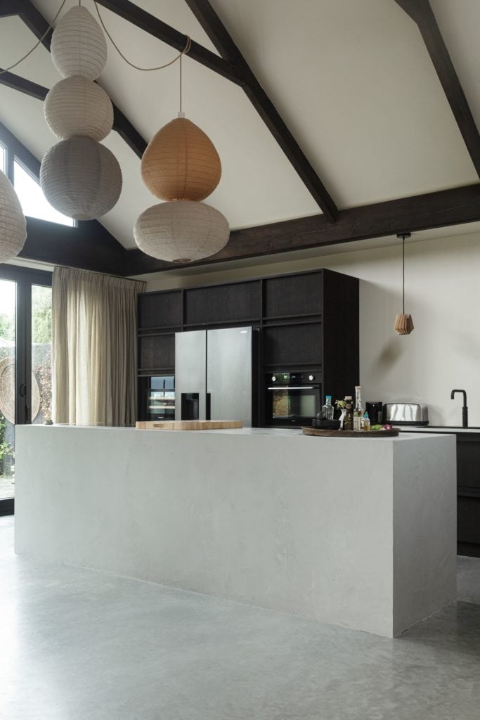 Zwarte keuken met een grijs kookeiland in Rijnburg. Hieronder ligt een gevlinderde betonvloer.