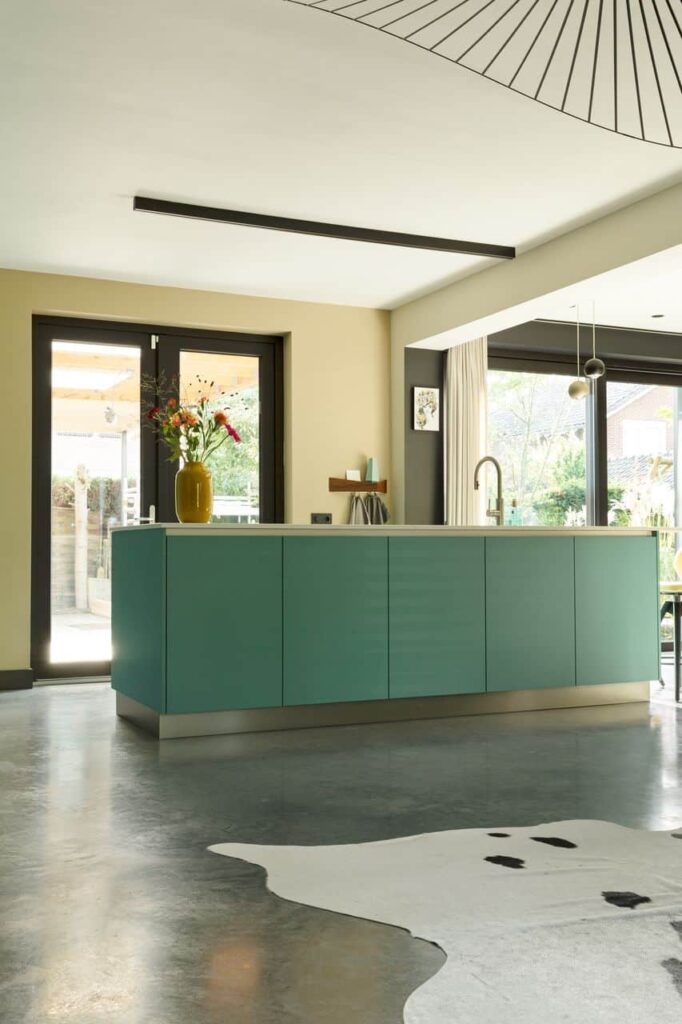 Turquoise kookeiland in de keuken in Venlo. Dit is gecombineerd met een gevlinderde betonvloer en daarop ligt een koeienhuid kleed.