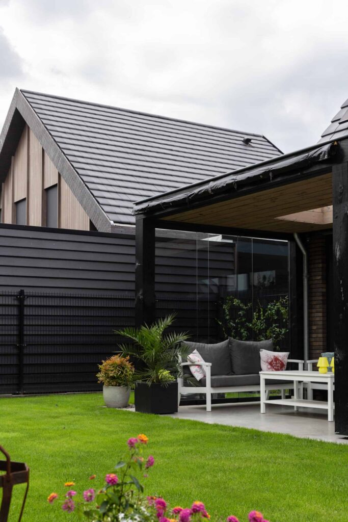 Terras onder een overkapping in Hilvarenbeek. Deze is gecombineerd met gras en op het terras staat een wit tuinset met grijze stoelen.