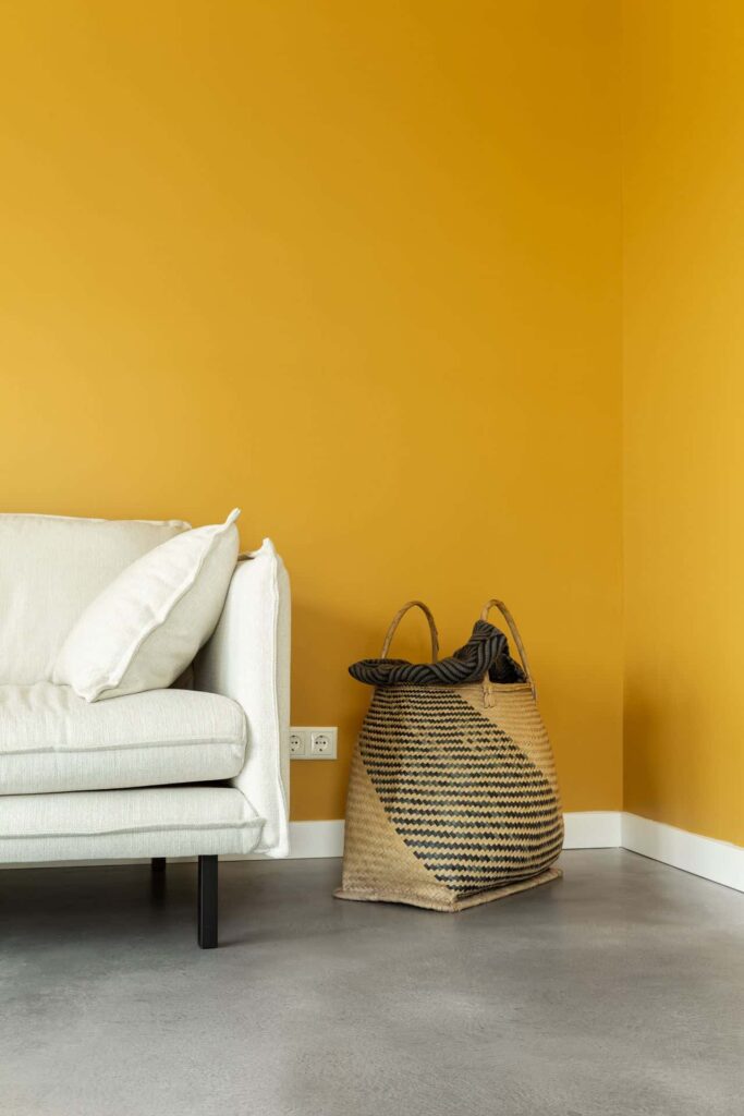 Italiaanse betonlook vloer in Voorhout met een gele wand en een witte bank. gietvloer Utrecht