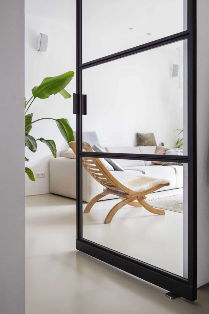 Woning in Zeist met een PU gietvloer van Willem Designvloeren, gecombineerd met stalen deuren, een beige bank, houten stoeltje en een grote plant.