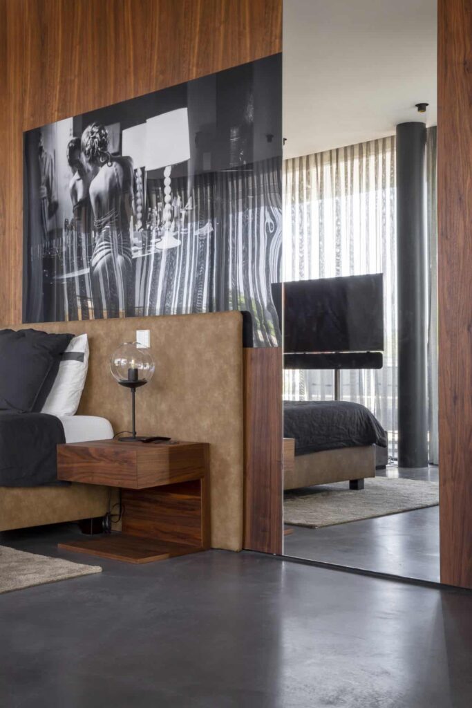 Gevlinderde woonbeton vloer in Warmond in de slaapkamer. De vloer is gecombineerd met een bruin bed en aan de wand hangt een groot zwart-witte foto van een vrouw.