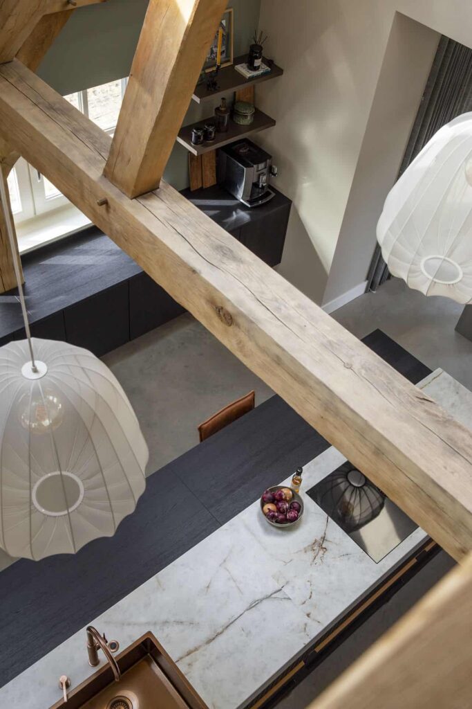 Foto van de houten balken aan het plafond de zwart met marmeren keuken en de gevlinderde betonvloer