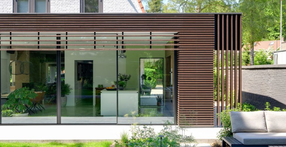 Foto van een moderne uitbouw aan een jaren '30 woning met houten lamellen op de gevel en grote glazen puien.