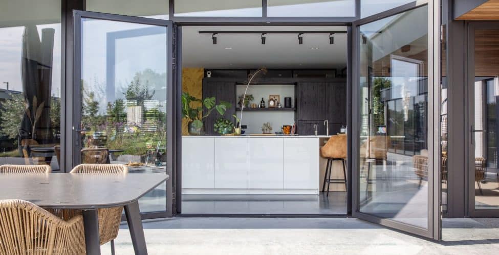 Een betonnen terras gecombineerd met een gevlinderde betonvloer voor binnen afgescheiden door een glazen pui met openslaande deuren.